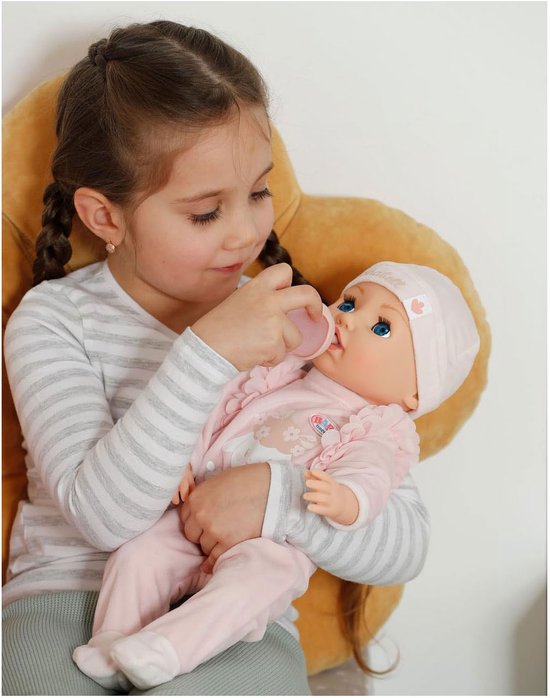 Meisje met vlechtjes voedt een baby Annabell pop met roze kleding en muts met een flesje.