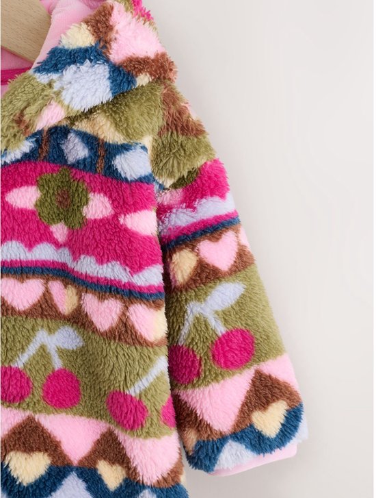 Close-up van de schouder en mouw van een fleece babyjasje met een kersen- en hartjespatroon.