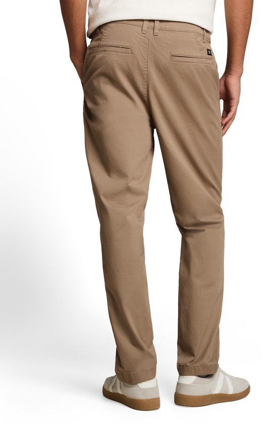 Achterkant van een beige chino, gedragen door een man met zijn handen in de zakken.