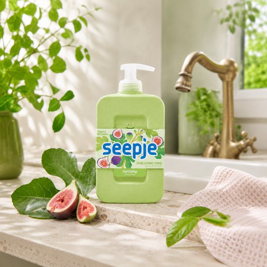 Lichtgroene fles Seepje handzeep op een aanrecht met verse vijgen, waterkraan en planten.