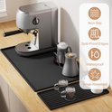 Zilverkleurige koffiemachine op een zwarte mat, met twee kannen, twee kleine glazen, en iconen voor anti-slip, lekvrije randen, waterdicht en slijtvast.