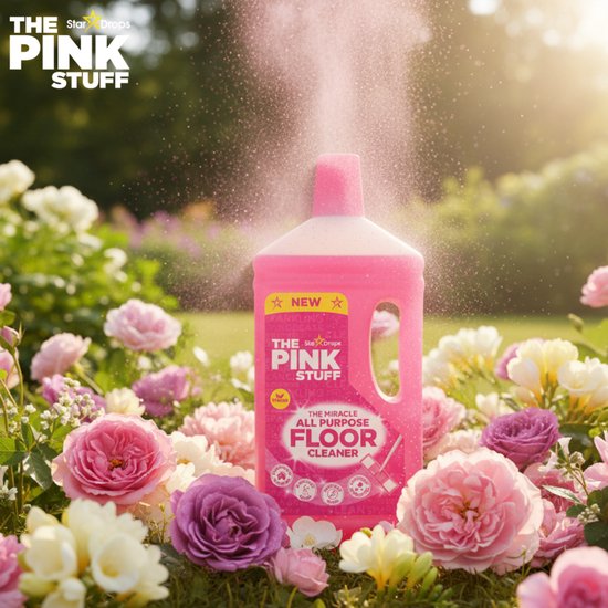 Fles The Pink Stuff vloerreiniger te midden van roze en witte bloemen in een tuin.