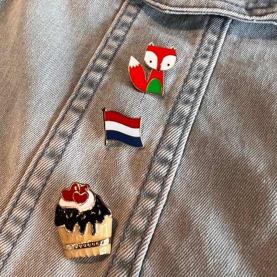 Drie pins op een spijkerjack: een vos, Nederlandse vlag en een cupcake met rode hartjes.