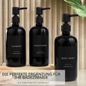 Drie zwarte pompdispensers met zwarte labels: SHAMPOO, CONDITIONER en BODY WASH. Staan op een houten plank.