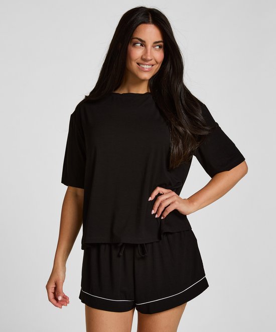 Model draagt een zwart pyjamashirt en een bijpassende short met witte bies.