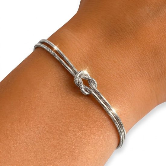Close-up van een zilverkleurige dubbele schakelarmband met knoopdetail, glinsterend op een huid.