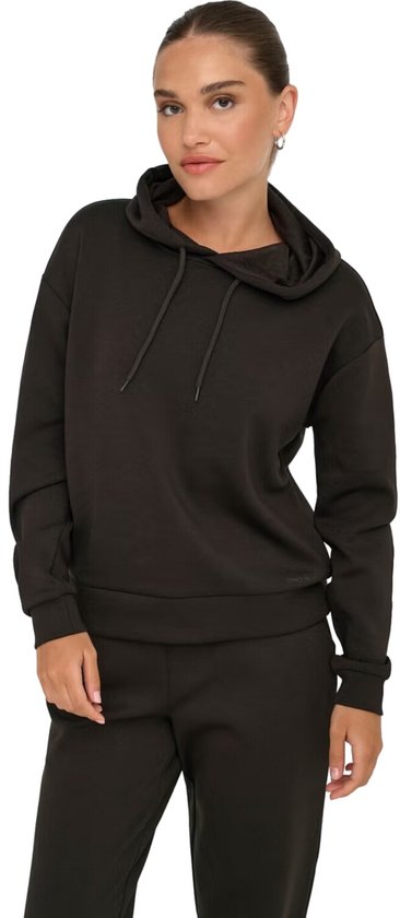 Model staat met de handen in de zakken in een donkerbruine hoodie en bijpassende joggingbroek.