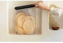 Main ouvrant le couvercle gris foncé d'une boîte transparente remplie de galettes de riz.