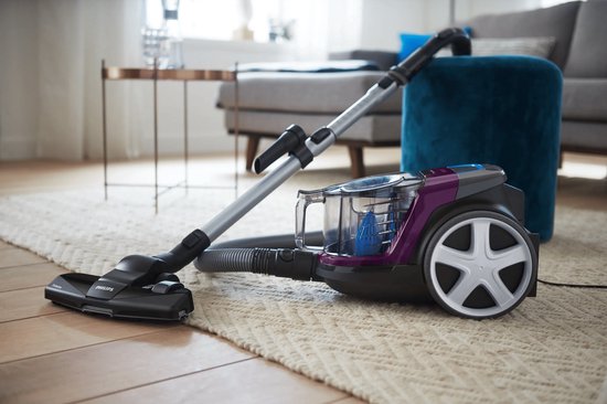 Aspirateur Philips PowerPro Compact violet en action sur un tapis dans un salon.