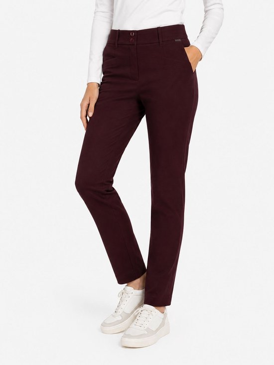 Model in een bordeauxrode broek met knoopsluiting en zakken, gedragen met een witte top.