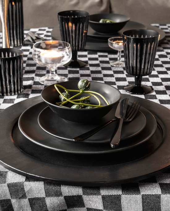 Gedekte tafel met zwart-wit geblokt tafeldoek, met daarop zwart servies, bestek, kandelaars, waxinelichtjes en groene decoratie.
