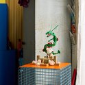 LEGO Rayquaza bouwpakket op een oranje platform. De groene draak met rode accenten en gouden ringen zweeft boven een platform met een figuur.