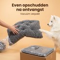 Hands schudden een grijs hondenkussen uit dat uit plastic komt.