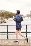 Homme portant une veste de sport bleue, un short noir, des chaussures noires et des chaussettes blanches, courant avec une bouteille bleue.