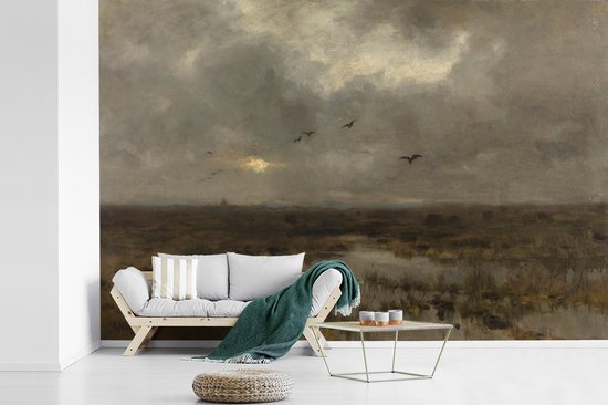 Un salon avec un canapé en bois clair et une table d'appoint, face à un tableau de marais avec un ciel nuageux.