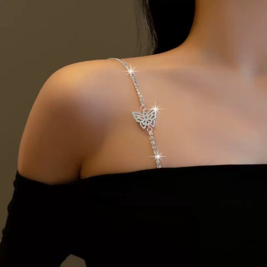 Model draagt zilverkleurige bh-bandjes met strass en vlinderdetail over de schouder, op een zwarte top.