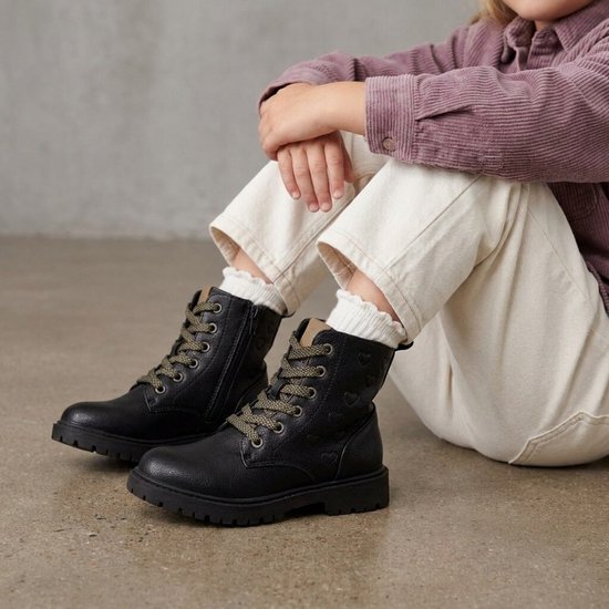 Zwart veterboots met groene veters en hartjesprint, gedragen door een kind op een betonnen vloer.