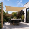 Een beige rechthoekig schaduwdoek hangt boven een tuintafel met stoelen.