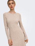 Model draagt een beige gebreide jurk met kabels en lange mouwen.