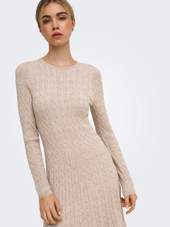 Model draagt een beige gebreide jurk met kabels en lange mouwen.