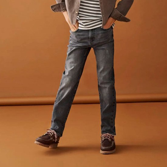 Jongen draagt donkergrijze jeans met rechte pijpen, met een gestreept shirt en bruine schoenen.