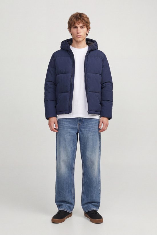 Model draagt een donkerblauwe pufferjack, open rits, met witte T-shirt en jeans.