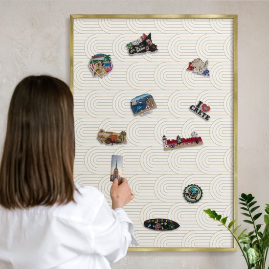 Een vrouw hangt een magneet op een magnetisch bord met gouden boogpatroon. Er hangen diverse stadsmagneten.