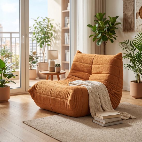 Oranje pluche zitzak met een plaid en boeken, in een lichte woonkamer.