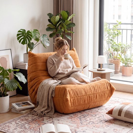 Vrouw leest een boek op een oranje pluche zitzak in een lichte woonkamer.