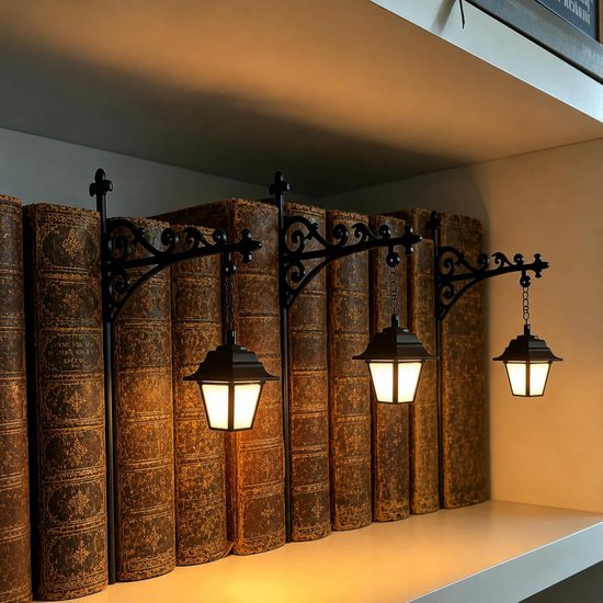 Drie zwarte metalen boekensteunen in de vorm van mini-lantaarns, die licht uitstralen tussen oude boeken.