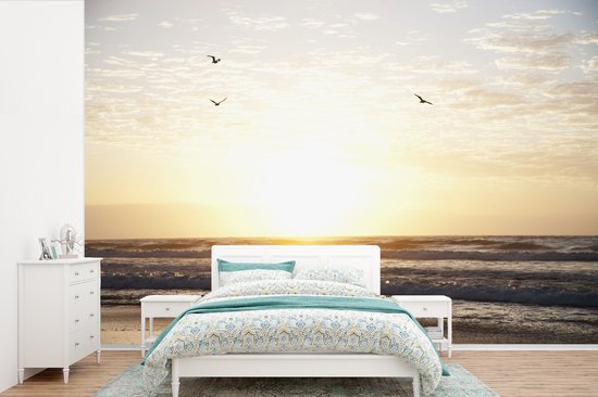 Chambre avec papier peint coucher de soleil, lit blanc avec parure bleue et commode blanche.