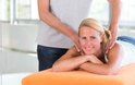 Een blonde vrouw ligt op haar buik op een oranje hoes terwijl een man haar nek masseert.