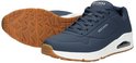 Deux sneakers Skechers bleu marine, l'une à l'envers, avec semelles blanches et semelles extérieures marron texturées.