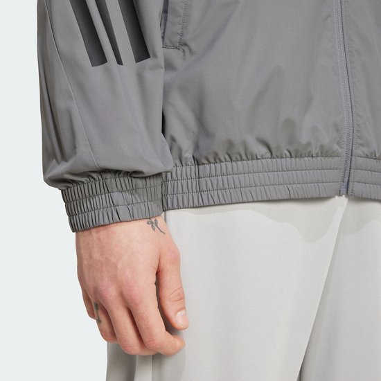 Detail van de zoom en mouw van een grijs Adidas trainingsjack met zwarte 3-strepen.