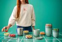 Tafel vol met Mepal producten, waaronder een groene lunchpot, een thermosbeker en diverse bakjes met fruit en muesli.