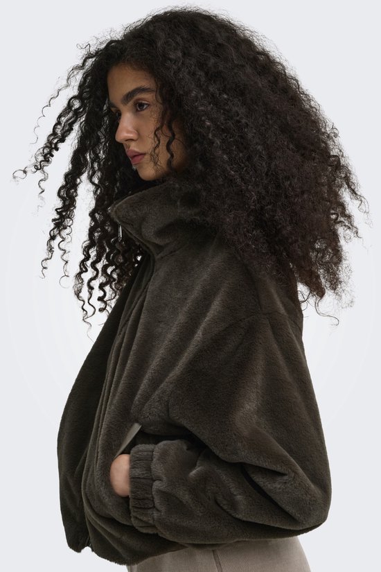 Model met krullend haar draagt een donkerbruine teddy jas met ritssluiting, zijaanzicht.