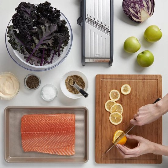 Een rauwe zalmfilet ligt op een bakplaat naast ingrediënten voor een salade, waaronder rode kool, groene appels, citroenschijfjes en donkere bladgroenten.