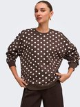 Model draagt een bruine sweater met witte polkadots, gecombineerd met een bruine broek.