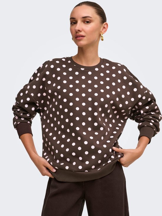 Model draagt een bruine sweater met witte polkadots, gecombineerd met een bruine broek.