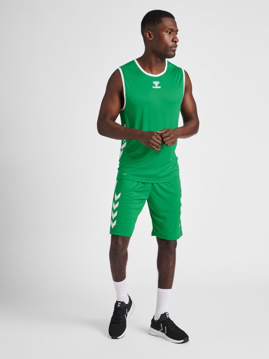 Model in een groene mouwloze sporttop met witte bies en bijpassende korte broek met witte chevrons. Zwarte schoenen en witte sokken.