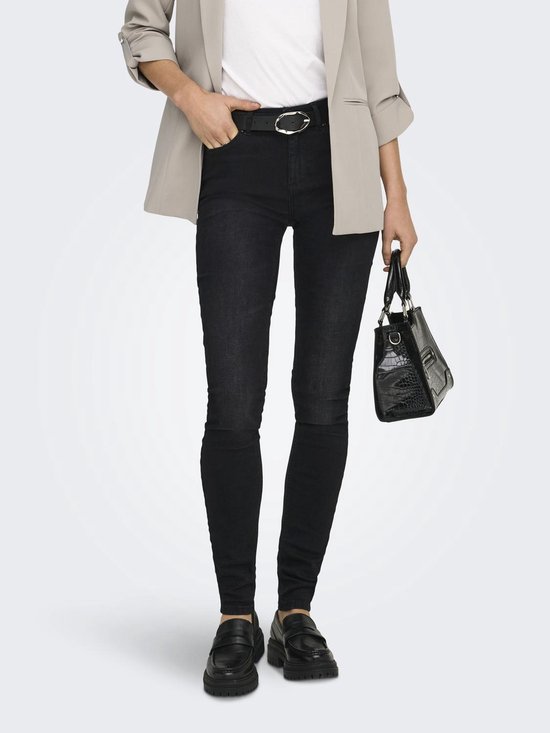 Model met beige blazer, zwarte skinny jeans, riem en handtas, van voren gezien.