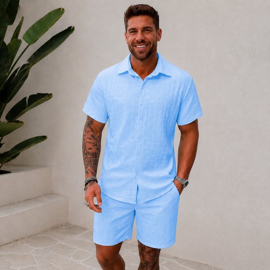 Man, vooraanzicht, draagt lichtblauwe korte mouw blouse en korte broek. Blouse met structuur.
