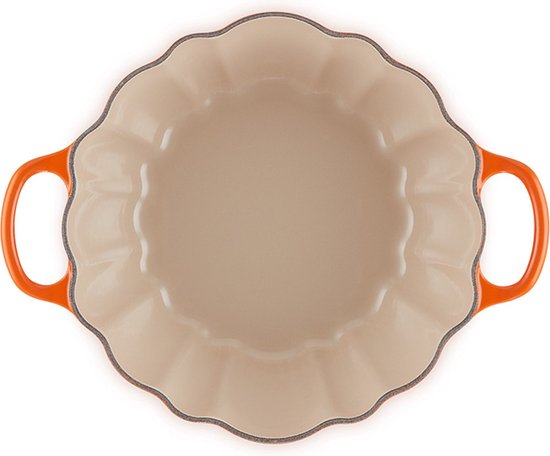 Binnenzijde van oranjerode pompoen braadpan met crèmekleurige binnenkant en golvende rand.
