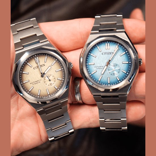 Twee Citizen horloges, zilverkleurig titanium, een met lichtblauwe wijzerplaat, de ander met bruinige wijzerplaat, op handen.