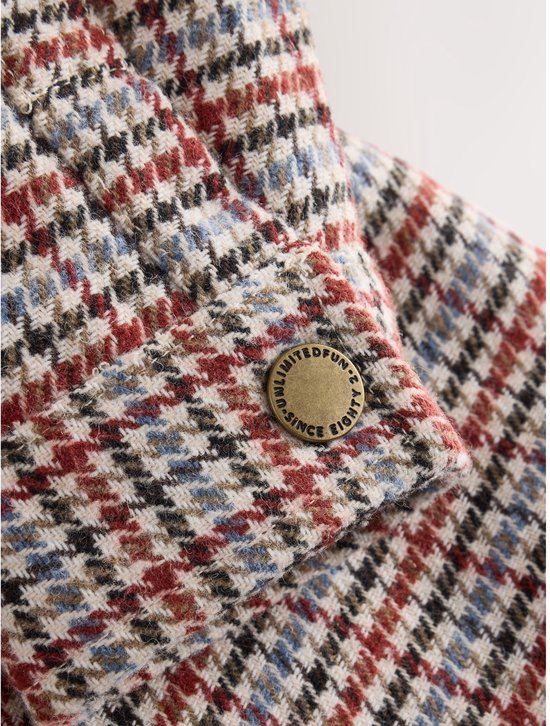 Close-up van de mouw met koperkleurige knoop met tekst 'Unlimited Fun Since Eighty'.