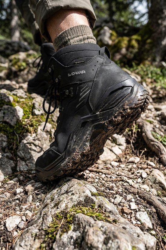 Een zwarte Lowa Renegade GTX wandelschoen met veters, Gore-Tex logo, gedragen op rotsachtig terrein.