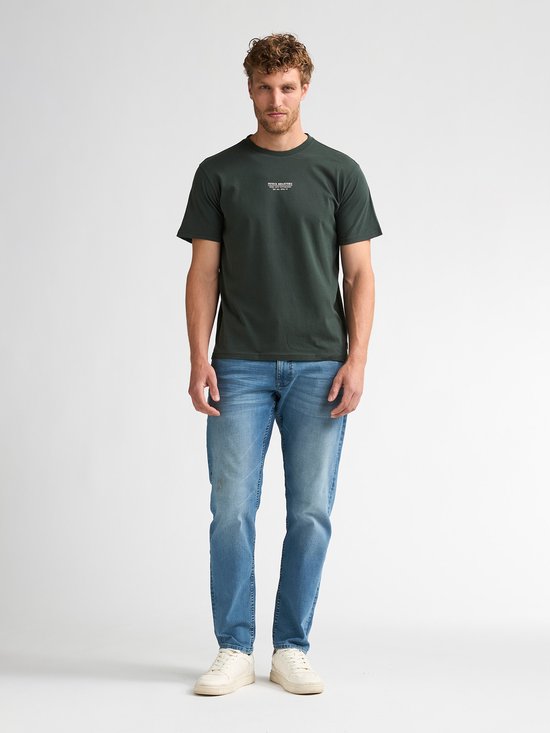 Man in donkergroen T-shirt met witte tekstprint en spijkerbroek. Heuplengte.
