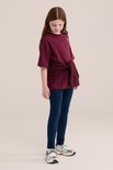 Meisje in donkerblauwe legging en bordeauxrood t-shirt met trui om de heupen.