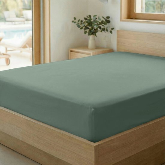 Drap-housse vert sauge sur un lit en bois avec un vase de plantes en arrière-plan.