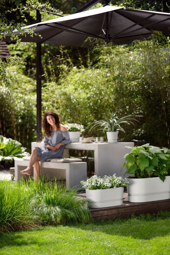 Vrouw in grijs jurkje zit op een betonnen tuinbank onder een parasol.